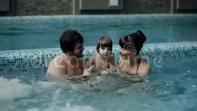 泳池里的年轻家庭。 父母带着儿子在游泳池里游泳和玩耍。
